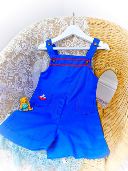 2-3 years. Royal blue short dungarees with red details, gold nautical buttons and pockets