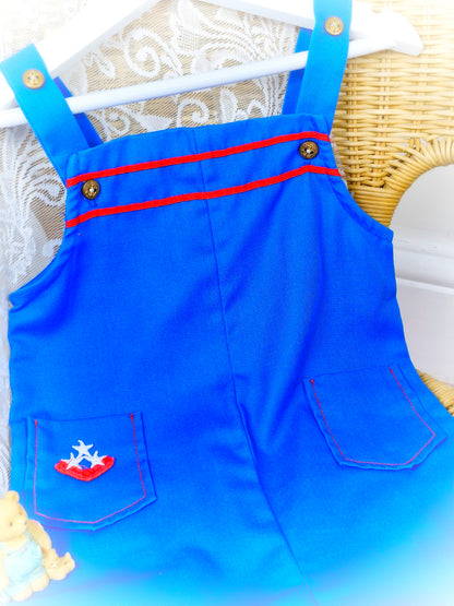 2-3 years. Royal blue short dungarees with red details, gold nautical buttons and pockets