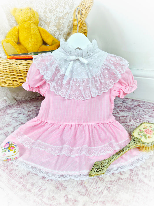 12-18 months. Pink vintage drop waist dress with high neck, white lace details and frilly bib