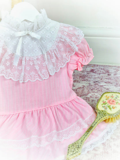 12-18 months. Pink vintage drop waist dress with high neck, white lace details and frilly bib