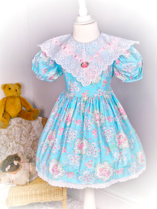 4 years. Bright blue vintage dress, Miss Victoria, with pink floral patters, white eyelet bib with pink rosette and satin ribbon