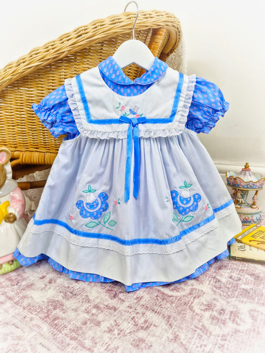 18-24 months/ 2 years. Two piece vintage dress, blue patterned dress with puff sleeves and white apron with blue trim and embroidered flowers