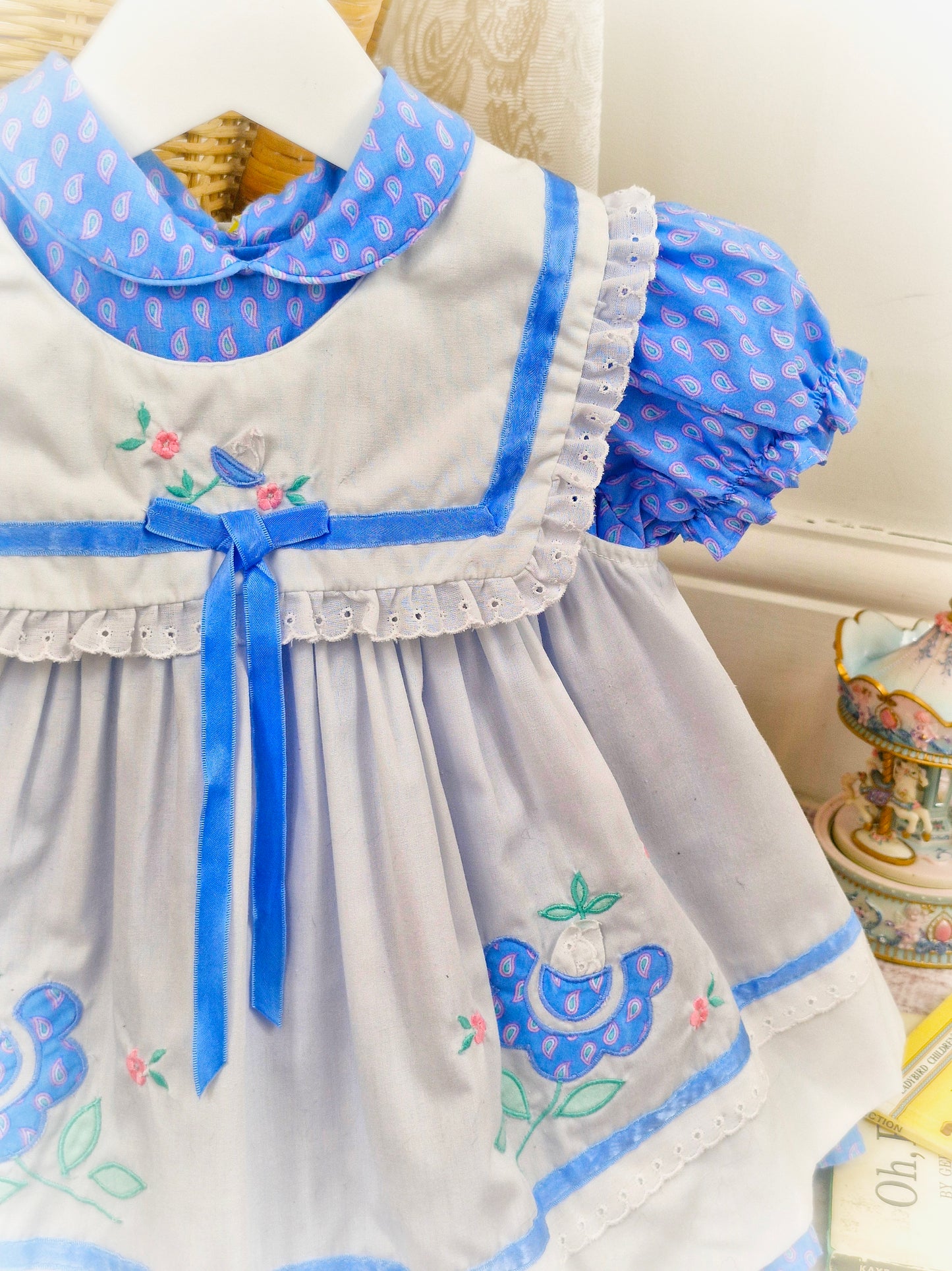 18-24 months/ 2 years. Two piece vintage dress, blue patterned dress with puff sleeves and white apron with blue trim and embroidered flowers