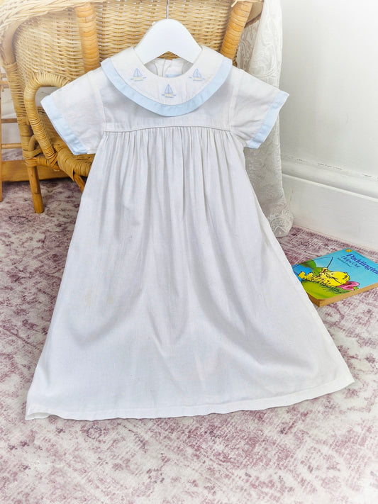 2 years. White vintage dress with blue trim and embroidered boats on bib. Maxi style.