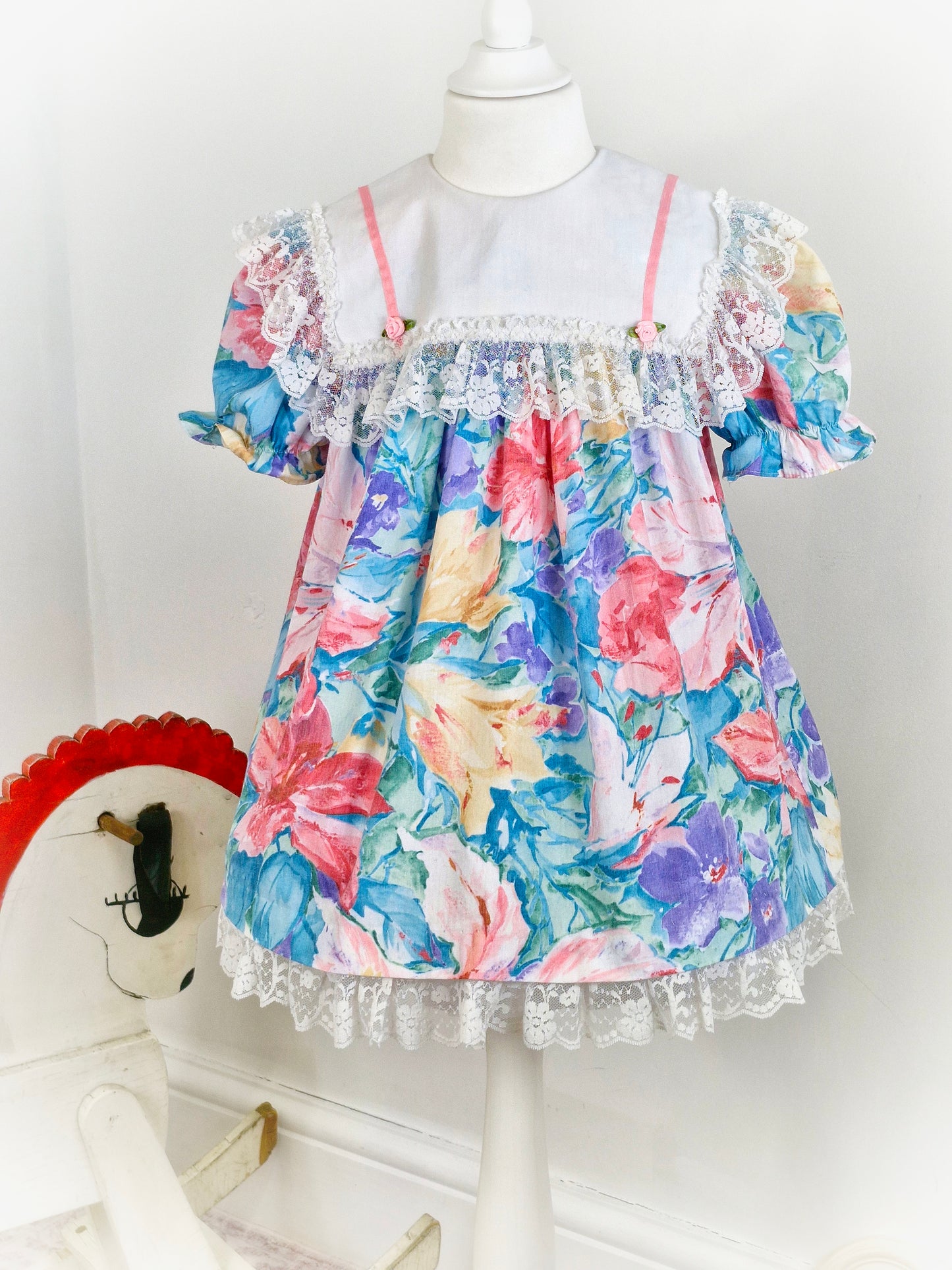 3-4 years. Watercolour printed vintage dress from Sandys Girls with large white bib, pink satin ribbon and rosettes and large lace trim