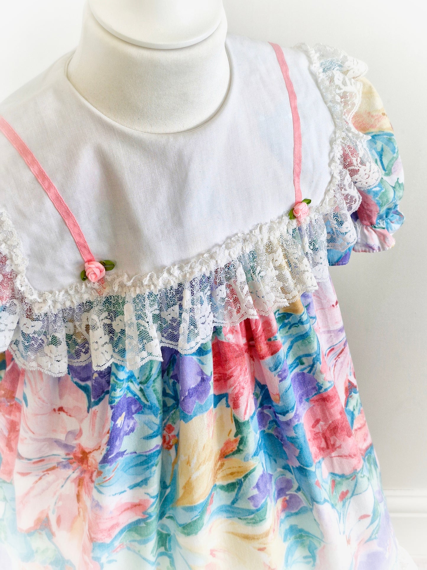 3-4 years. Watercolour printed vintage dress from Sandys Girls with large white bib, pink satin ribbon and rosettes and large lace trim