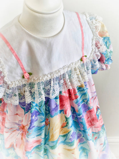 3-4 years. Watercolour printed vintage dress from Sandys Girls with large white bib, pink satin ribbon and rosettes and large lace trim