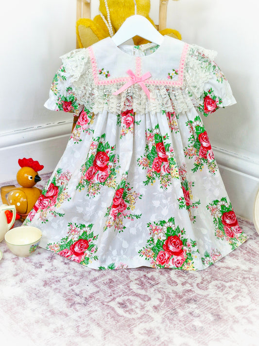 3 years. Vintage floral dress with white bib trimmed with lace and pink satin ribbon