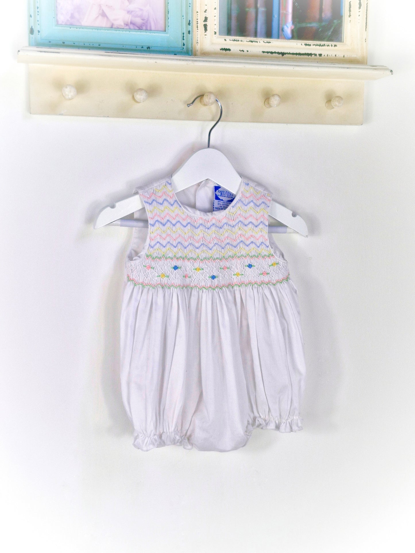 6-9 months. White sleeveless romper with smocking embroidered with pink, blue and lemon zigzags and flowers. Carriage Boutique
