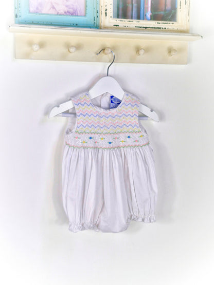 6-9 months. White sleeveless romper with smocking embroidered with pink, blue and lemon zigzags and flowers. Carriage Boutique