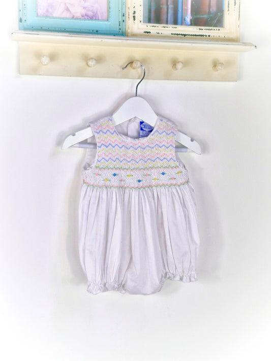 6-9 months. White sleeveless romper with smocking embroidered with pink, blue and lemon zigzags and flowers. Carriage Boutique