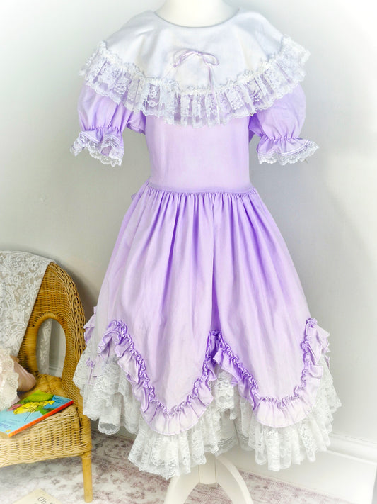 12-14 years. Lilac Lid'l Dolly with white bib, puff sleeves and lace trim