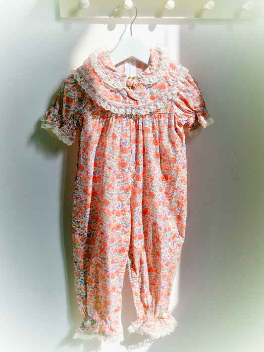 12-18 months. Peach floral romper with lace cuffed sleeves and ankles, ruffled bib and puff sleeves