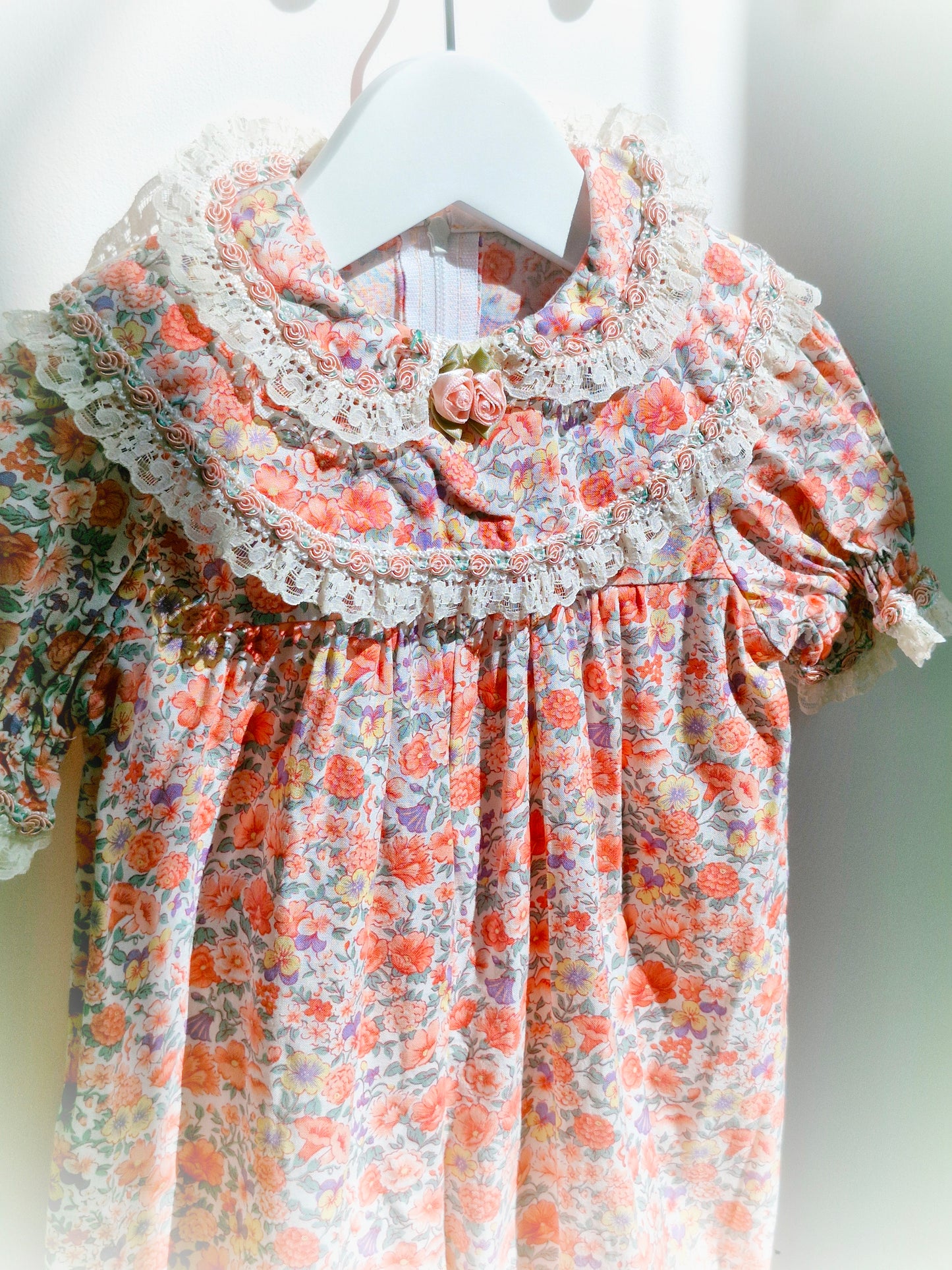 12-18 months. Peach floral romper with lace cuffed sleeves and ankles, ruffled bib and puff sleeves