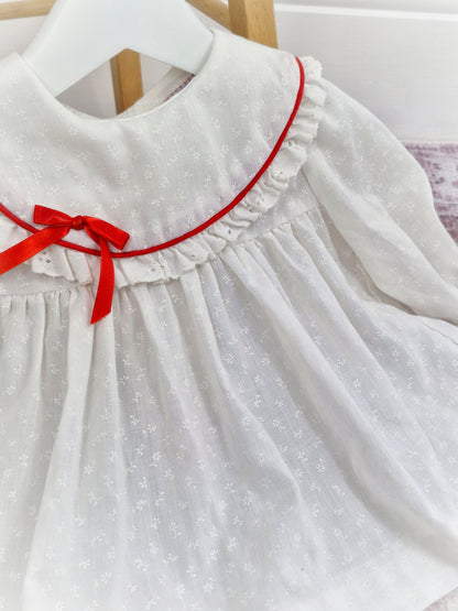 6-9 months. White vintage dress with long sleeves, white floral print, red ribbon and eyelet trimmed bib