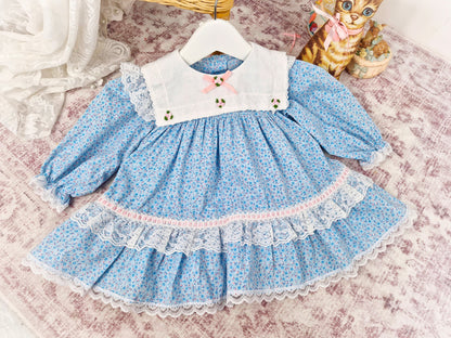 9-12 months. Blue floral vintage dress with white bib and lace, pink satin ribbon and rosettes