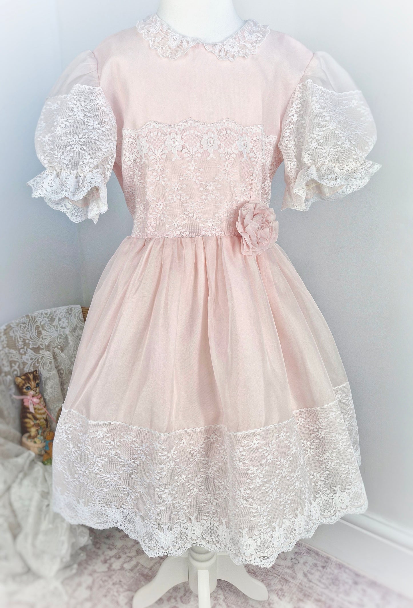 7-8 years. Light pink vintage organza dress with puff sleeves, white lace details and a floral accent at the waist.