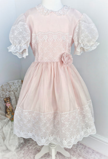 7-8 years. Light pink vintage organza dress with puff sleeves, white lace details and a floral accent at the waist.