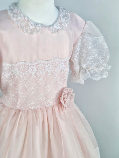 7-8 years. Light pink vintage organza dress with puff sleeves, white lace details and a floral accent at the waist.
