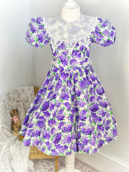 7-8 years. White vintage dress from Jayne Copeland with purple and green floral design, large white bib and puff sleeves