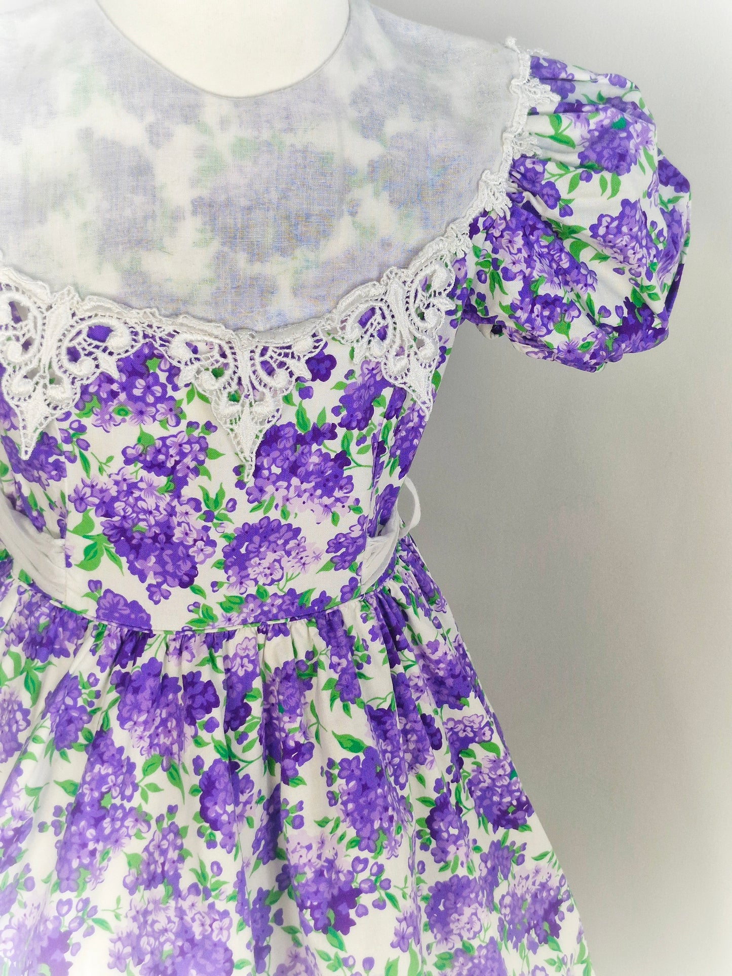 7-8 years. White vintage dress from Jayne Copeland with purple and green floral design, large white bib and puff sleeves