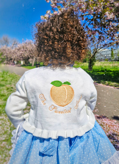 Frilly cream knit bolero with The Sweetest Peach embroidered on the back
