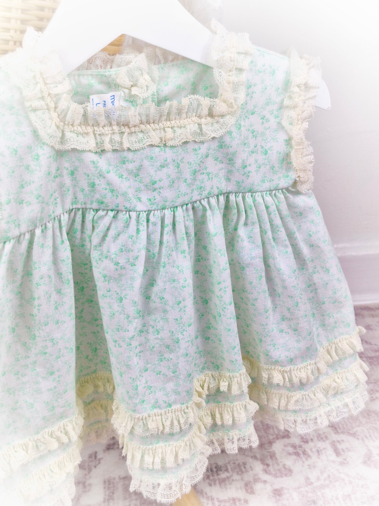 6-9 months. Vintage sleeveless Miniworld dress with green floral patterns and cream coloured lace