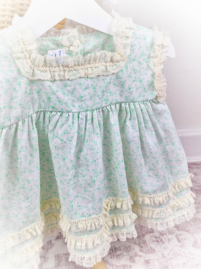 6-9 months. Vintage sleeveless Miniworld dress with green floral patterns and cream coloured lace