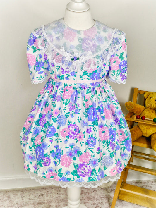 4-5 years. White vintage Celeste dress with pink and purple floral design and large white lace bib