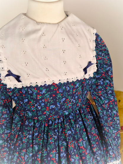 7-8 years. Navy floral vintage dress with long sleeves, white eyelet bib and satin bows. Deadstock