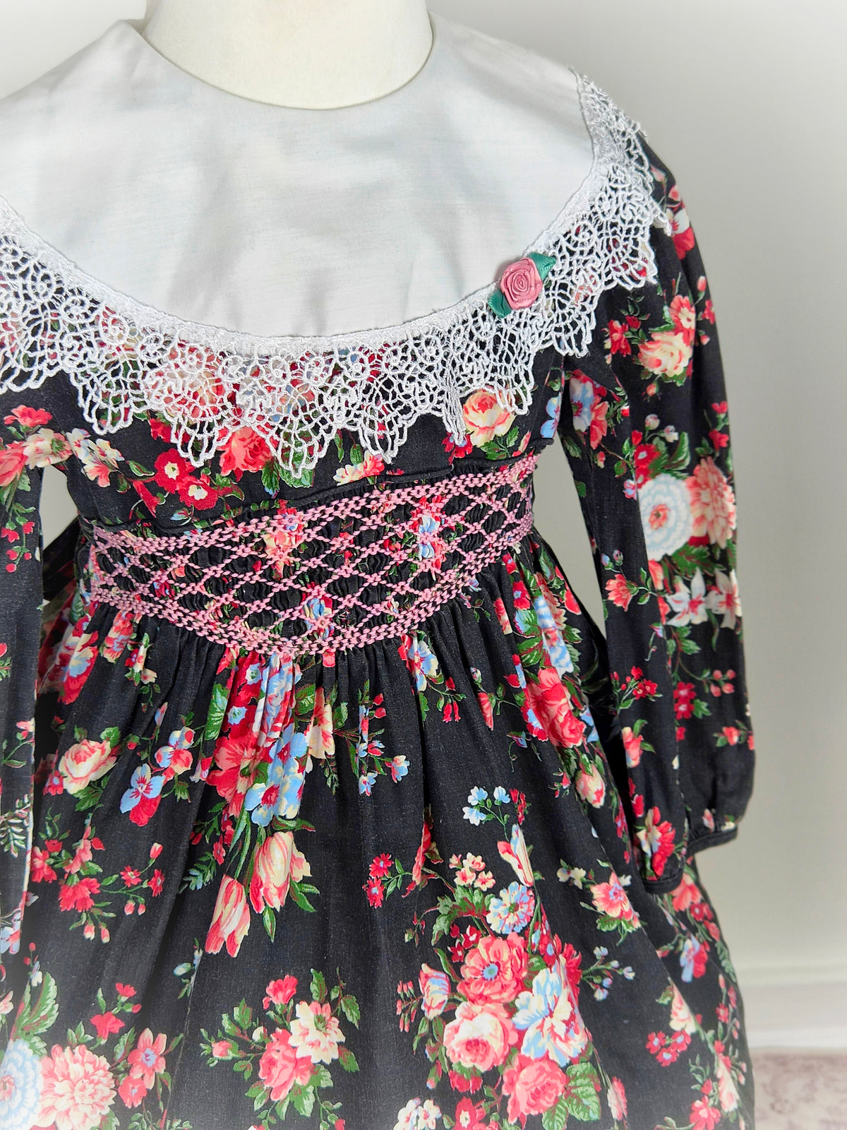 2-3 years. Black floral Polly Flinders smock dress with pink embroidery, white bib with lace trim and pink rosette