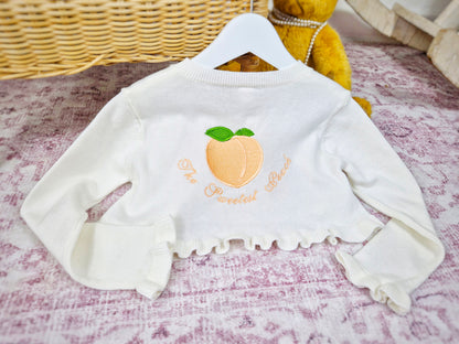 Frilly cream knit bolero with The Sweetest Peach embroidered on the back