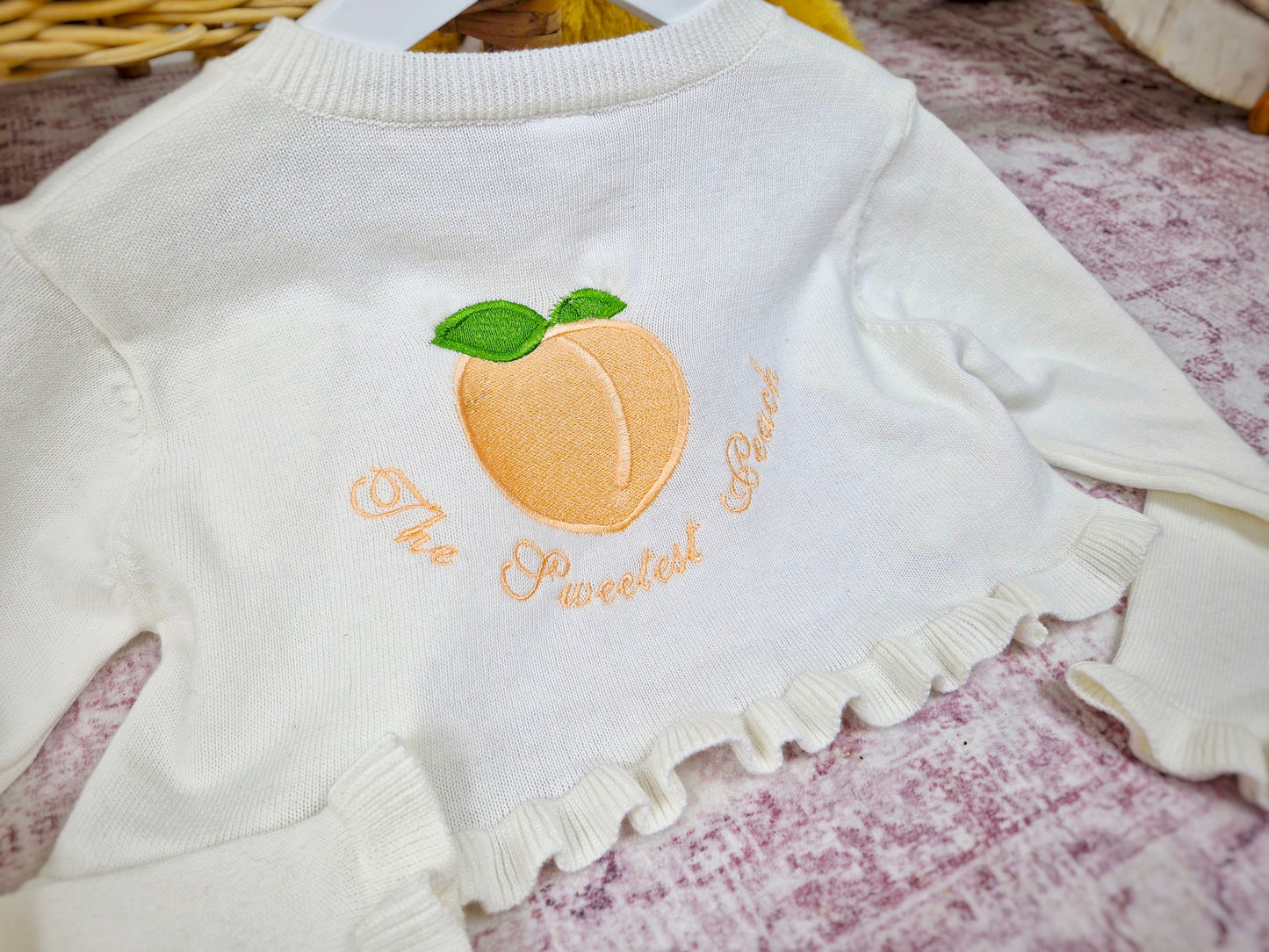 Frilly cream knit bolero with The Sweetest Peach embroidered on the back