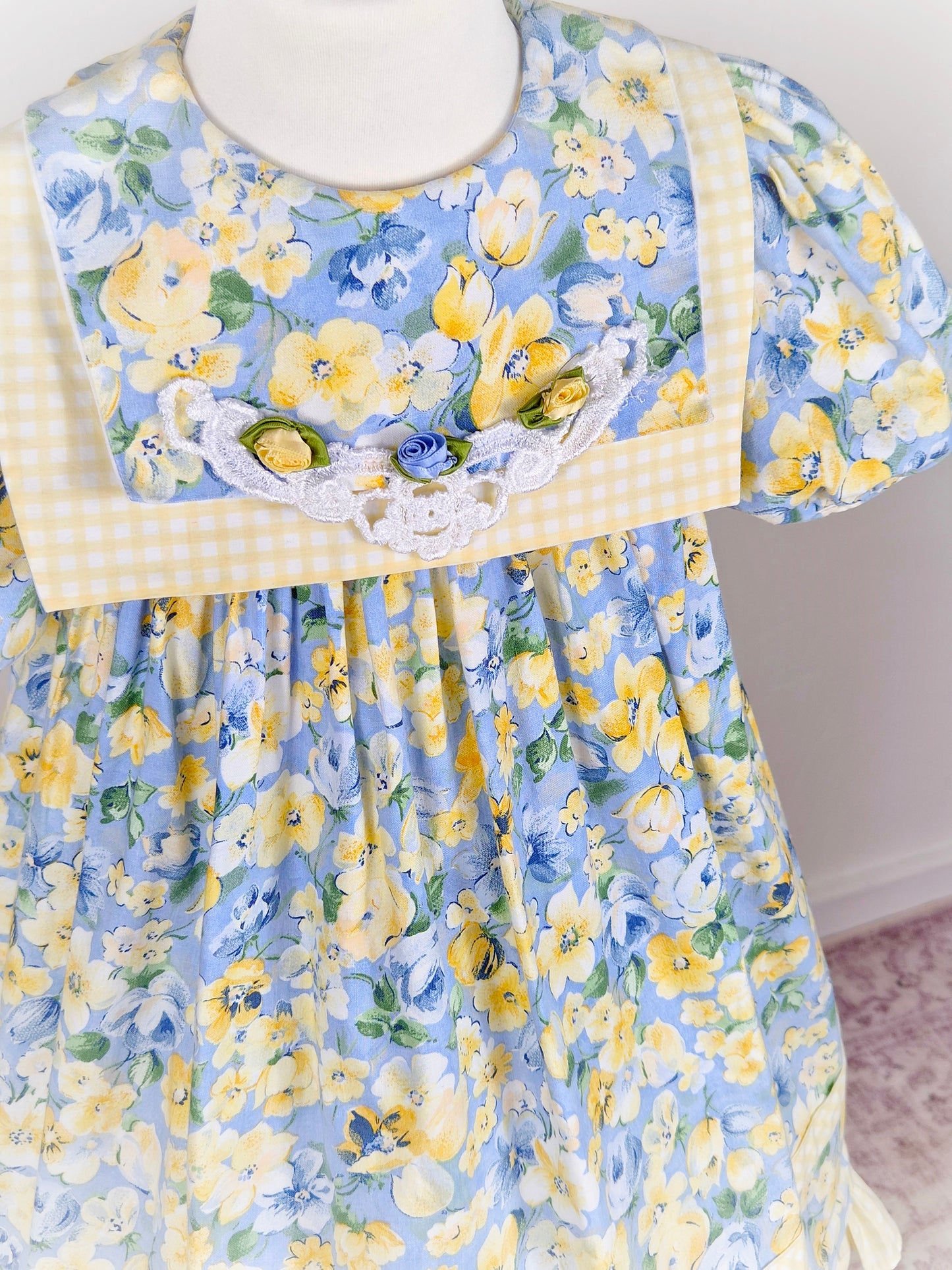 6-7 years. Blue and lemon floral vintage dress from Rare Editions with lemon and white gingham trim and three rosettes