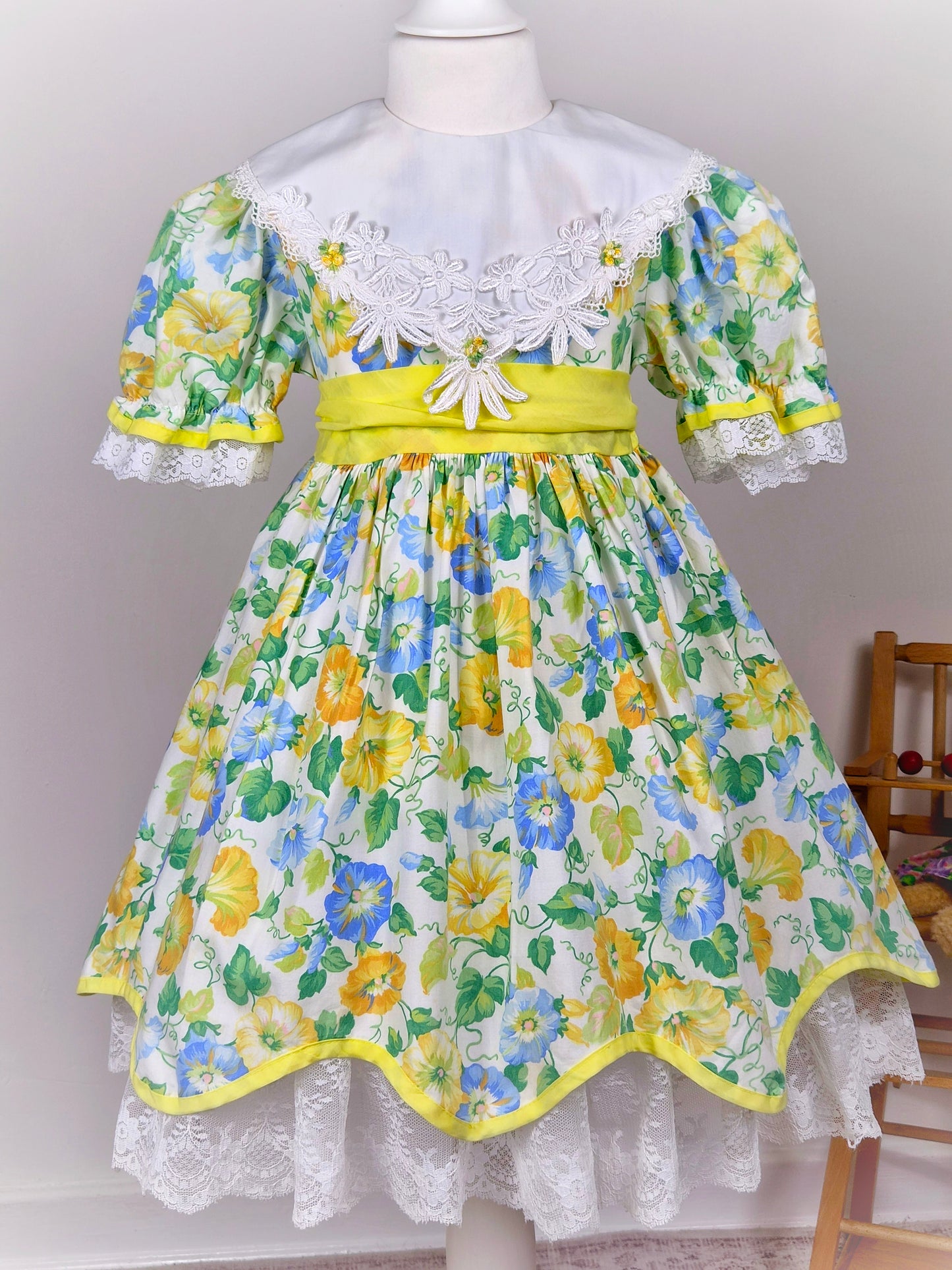 4-5 years. Vintage floral dress, yellow, blue and green with large white bib, yellow belt and rosettes and white lace hem