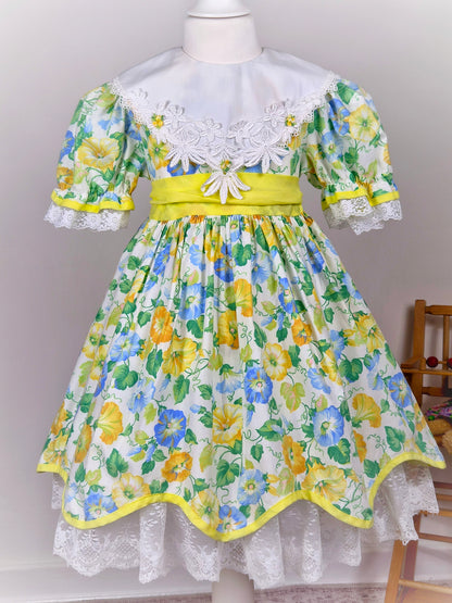 4-5 years. Vintage floral dress, yellow, blue and green with large white bib, yellow belt and rosettes and white lace hem