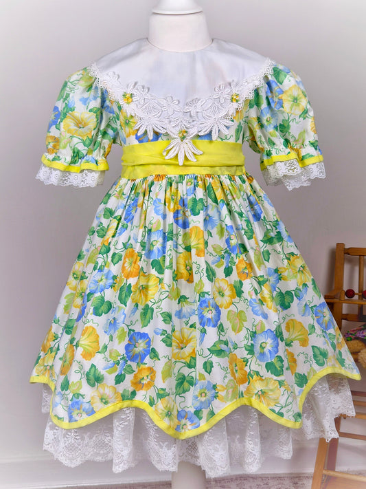 4-5 years. Vintage floral dress, yellow, blue and green with large white bib, yellow belt and rosettes and white lace hem