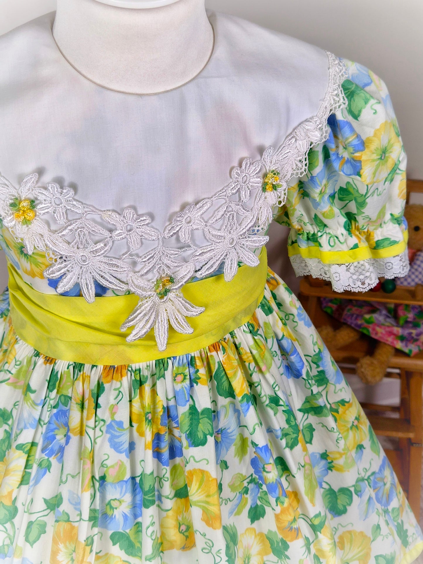 4-5 years. Vintage floral dress, yellow, blue and green with large white bib, yellow belt and rosettes and white lace hem
