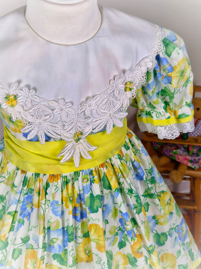4-5 years. Vintage floral dress, yellow, blue and green with large white bib, yellow belt and rosettes and white lace hem