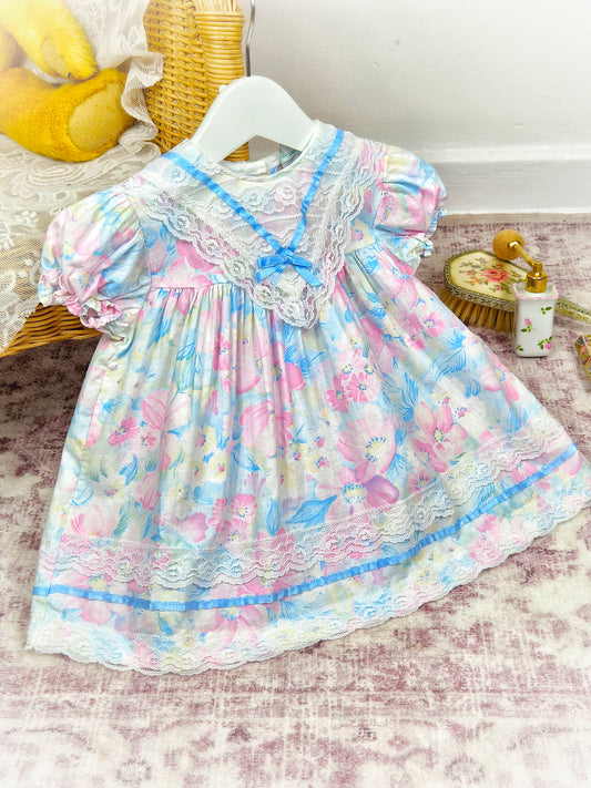 12-18 months. Pastel coloured floral vintage dress with lace bib and blue satin ribbon