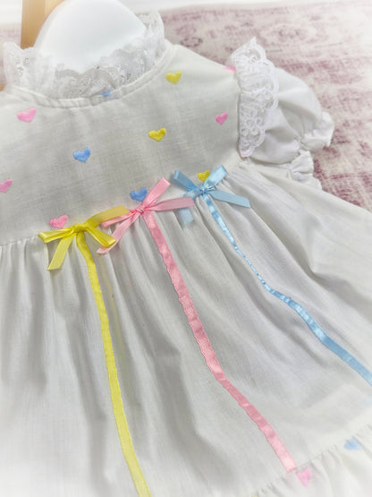 9-12 months. White vintage dress with pink, blue and lemon embroidered hearts and satin ribbons and bows