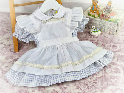9-12 months. White and blue checked dress with white apron and frilly shoulders