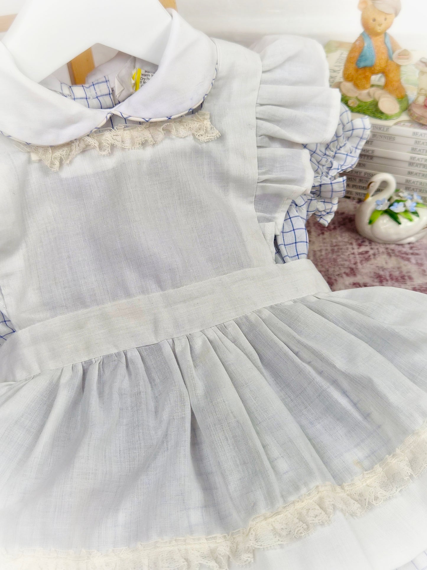 9-12 months. White and blue checked dress with white apron and frilly shoulders