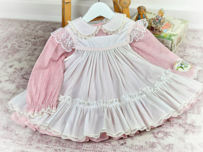18-24 months. Two piece vintage Bryan, pink floral dress with white frilly apron trimmed with white lace and pink satin ribbon