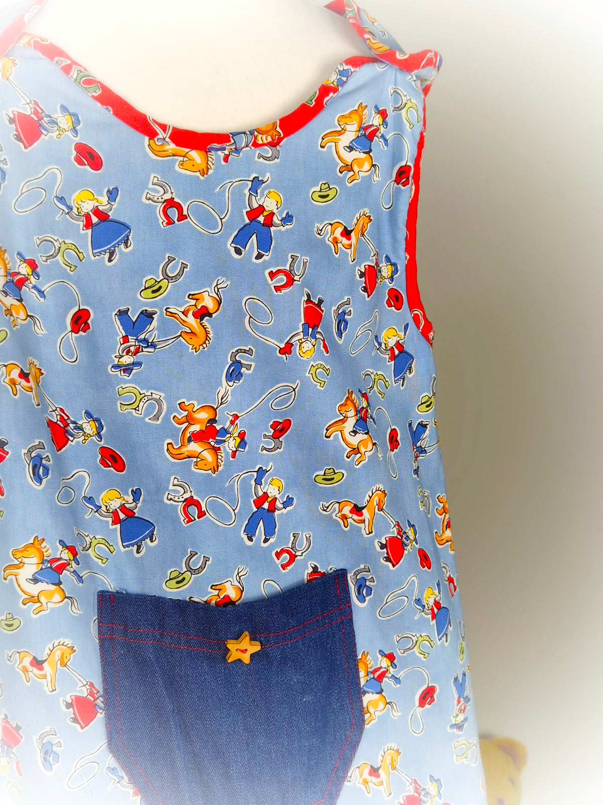 5-6 years. Blue and red handmade sleeveless dress with cowboys print, denim pocket and star button