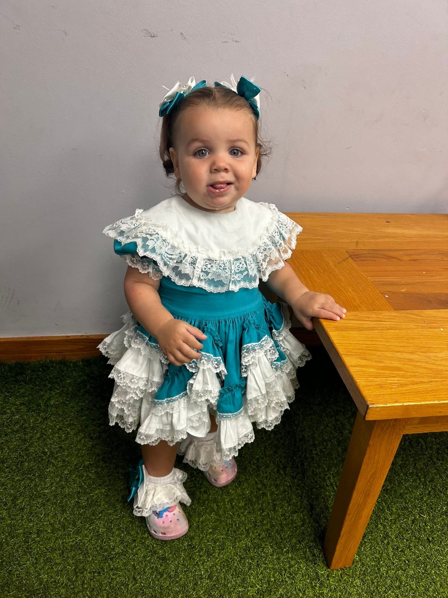 6-12 months. Teal Lid'l Dolly with white ruffles, lace and bib