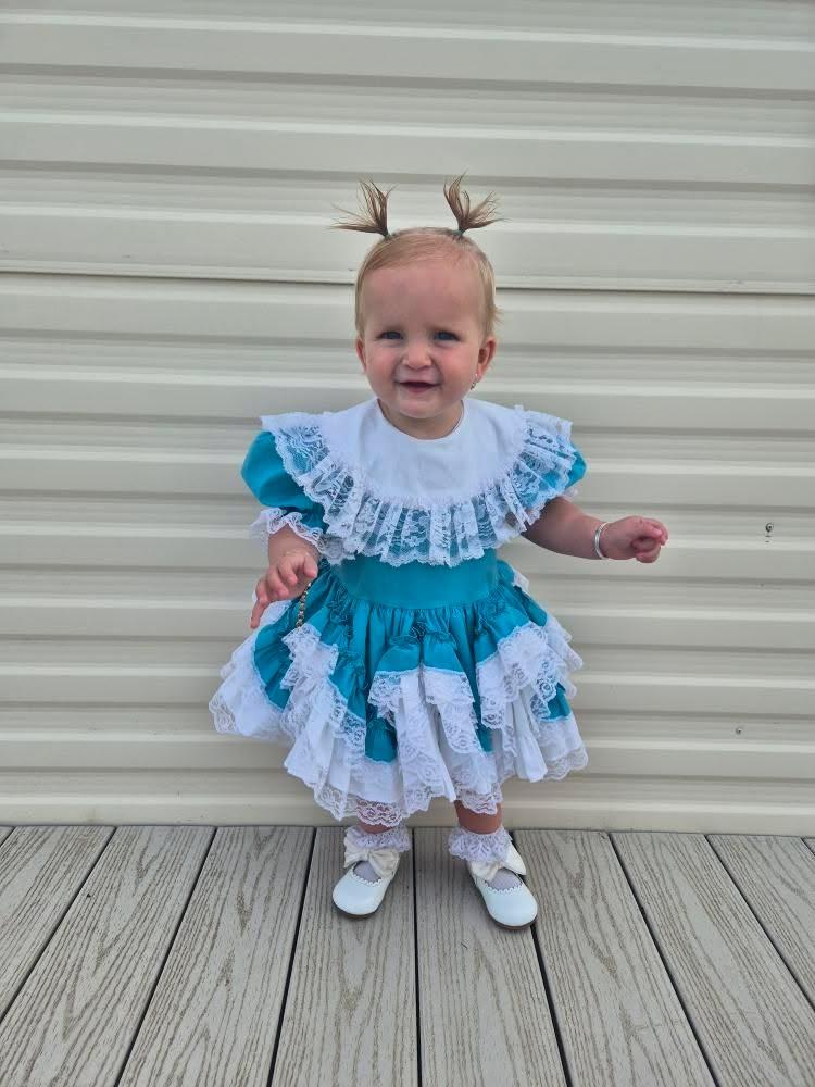 6-12 months. Teal Lid'l Dolly with white ruffles, lace and bib