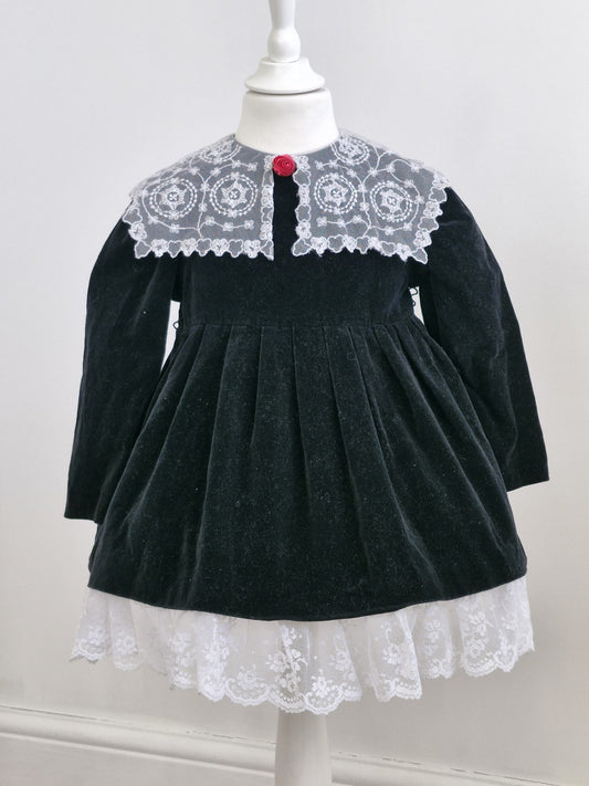 3-4 years. Black velvet vintage dress with white lace hem & collar and pink flower centre.