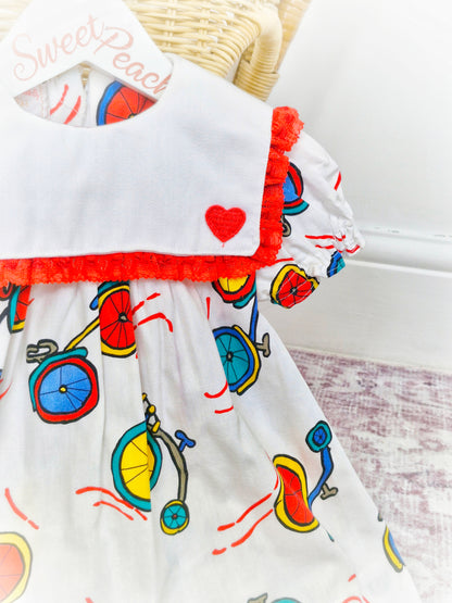 12-18 months. White handmade dress with red hearts and lace on bib and bicycle print