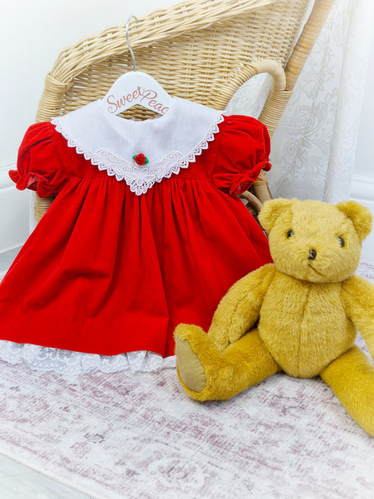 12-18 months. Red velvet dress with white bib and lace and a rosette. Hugs & Kisses